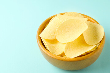 Tasty potato chips in bowl on light blue background, closeup. Space for text