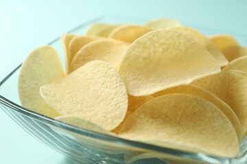 Tasty potato chips on light blue background, closeup
