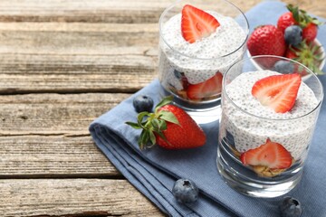 Delicious dessert with chia seeds, yogurt, strawberries and blueberries on wooden table, closeup...
