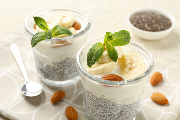 Delicious dessert with chia seeds, yogurt, banana, almond and mint in glasses on table, closeup. Superfood