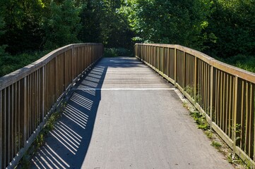 Fototapeta premium Wooden bridge with shadows stretching across the asphalt path in a park