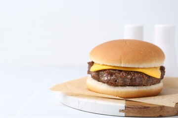 Tasty cheeseburger on white table, closeup. Space for text