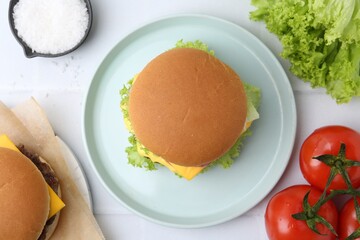 Tasty cheeseburger and ingredients on white table, flat lay