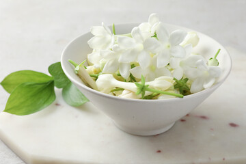 Beautiful jasmine flowers in bowl and green leaves on table, closeup
