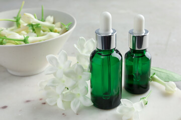 Bottles of essential oils and jasmine flowers on table, closeup