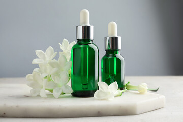 Bottles of essential oils and jasmine flowers on light grey table, closeup