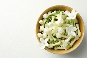 Beautiful jasmine flowers in bowl on white table, top view. Space for text
