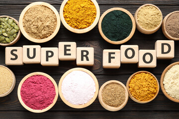 Different superfoods and words made of cubes on wooden table, flat lay
