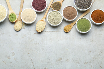 Different superfood powders in spoons and bowls on grey textured table, flat lay. Space for text
