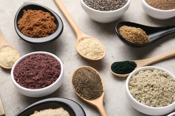Different superfood powders in spoons and bowls on grey textured table