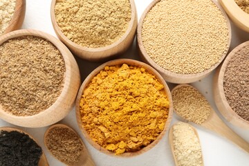 Different superfood powders in bowls and spoons on white background, flat lay