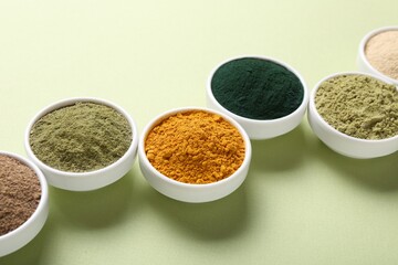 Different superfood powders in bowls on pale green background, closeup
