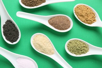 Different superfood powders in spoons on green background, flat lay