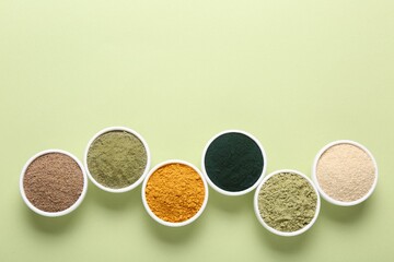 Different superfood powders in bowls on pale green background, flat lay. Space for text