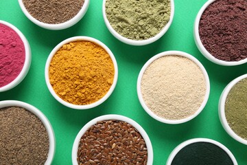 Different superfood powders in bowls on green background, flat lay