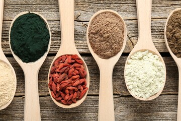 Different superfoods in spoons on wooden table, flat lay