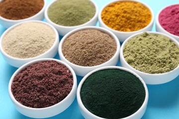 Different superfood powders in bowls on light blue background, closeup