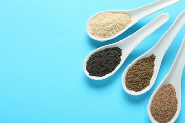 Different superfood powders in spoons on light blue background, flat lay. Space for text