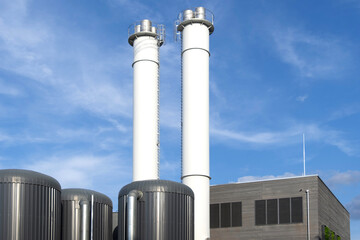 Two towering white chimneys against blue sky dominate skyline of industrial complex. symbol manufacturing and industry, modern industrial facility
