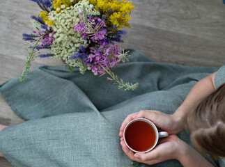 Holding a warm beverage while surrounded by fresh flowers in a cozy indoor setting