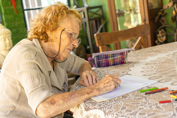 Elderly woman drawing with crayons at home: engaging in creative activities during retirement