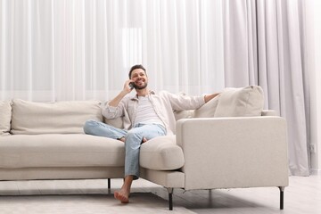 Fototapeta premium Man talking smartphone near window with beautiful curtains in living room