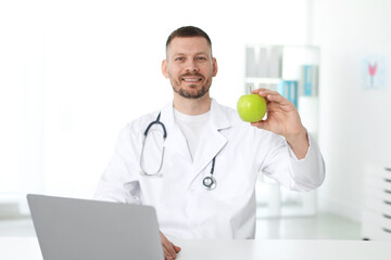 Nutritionist with green apple and stethoscope in clinic, selective focus