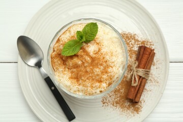 Delicious rice pudding with cinnamon, mint and spoon on white wooden table, top view