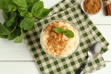 Delicious rice pudding with cinnamon, mint and spoon on white wooden table, flat lay