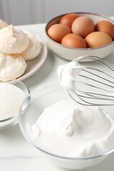Whisk with whipped cream and other ingredients on light table, closeup. Cooking meringue cookies