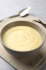 Tasty vanilla pudding in bowl, pods and spoon on light grey table, closeup
