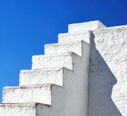 Exterior white steps against a vivid blue sky.  A low angle view of a series of steps,  crafted from white stucco, rising towards the sky.  Shadows are cast on the wall