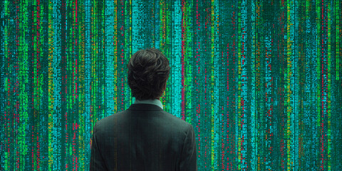 Man in suit viewing colorful data stream wall, representing data analysis, technology, or coding concept