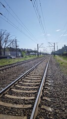 Fototapeta premium Railroad tracks with electric wires running through an urban area under clear sky. Concept of transportation, movement and industrial infrastructure in everyday environment