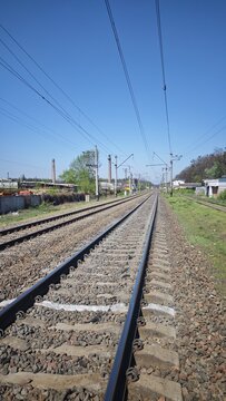 Railway tracks stretching into the distance under a clear blue sky with overhead power lines. Concept of travel, connection, infrastructure and forward journey
