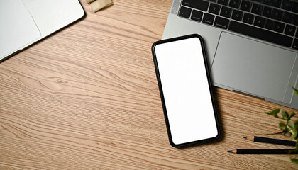 the scene is a flat lay of a light brown wooden surface. a mobile device with a white screen sits towards the center, partially obscuring the corner of a laptop computer