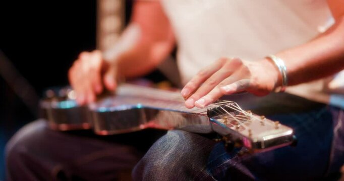 a close up of a guitarist playing slide guitar on their lap