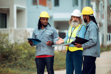 Construction engineers and their team are discussing the site preparation plan for installing solar panels, setting up the working system for an energy-saving housing project and exterior overview.