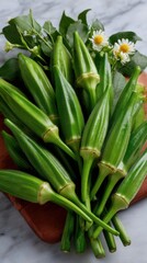 Obraz premium Fresh Green Okra Pods and Flowers on Wooden Cutting Board on Marble Surface