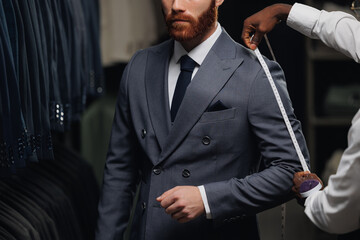 Professional tailor measuring customer for bespoke suit in menswear store