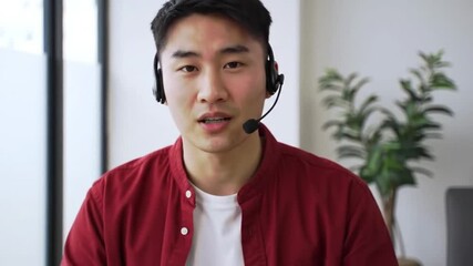 Asian man wearing headset in a video call, providing customer support with friendly and professional demeanor.