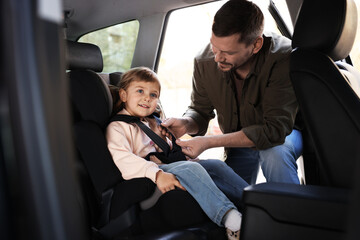 Happy father fastening her daughter in child safety seat inside car