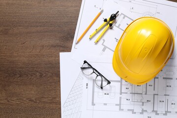 Different architectural drawings, hard hat, pencil, divider and glasses on wooden table, flat lay....