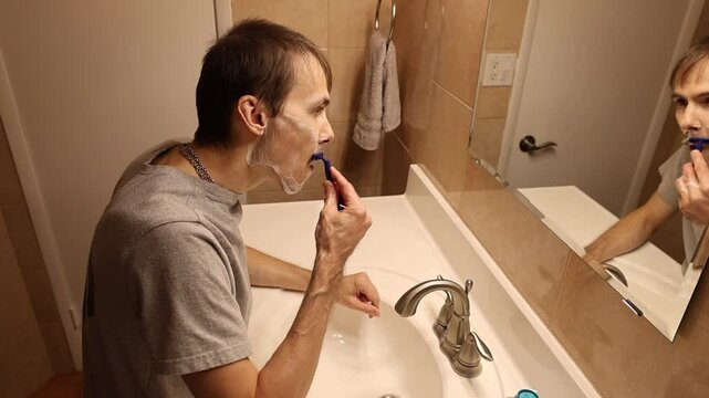 A man shaves his face using a razor. The razor glides smoothly over his skin, removing stubble, with clear focus on the motion of the blade and the details of his face during the shave.
