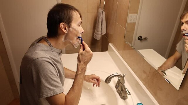 A man shaves his face using a razor. The razor glides smoothly over his skin, removing stubble, with clear focus on the motion of the blade and the details of his face during the shave.