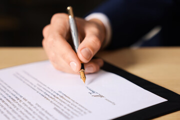 Man putting signature on document at table, closeup