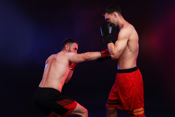 Men in boxing gloves fighting on dark background with smoke