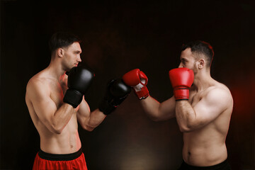 Men in boxing gloves fighting on dark background with smoke
