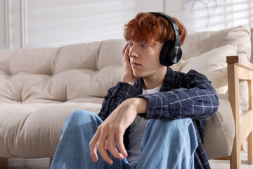 Obraz premium Teen problems. Depressed teenage boy listening to music on floor at home, space for text