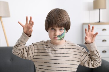 Cute boy with dinosaur face painting posing indoors